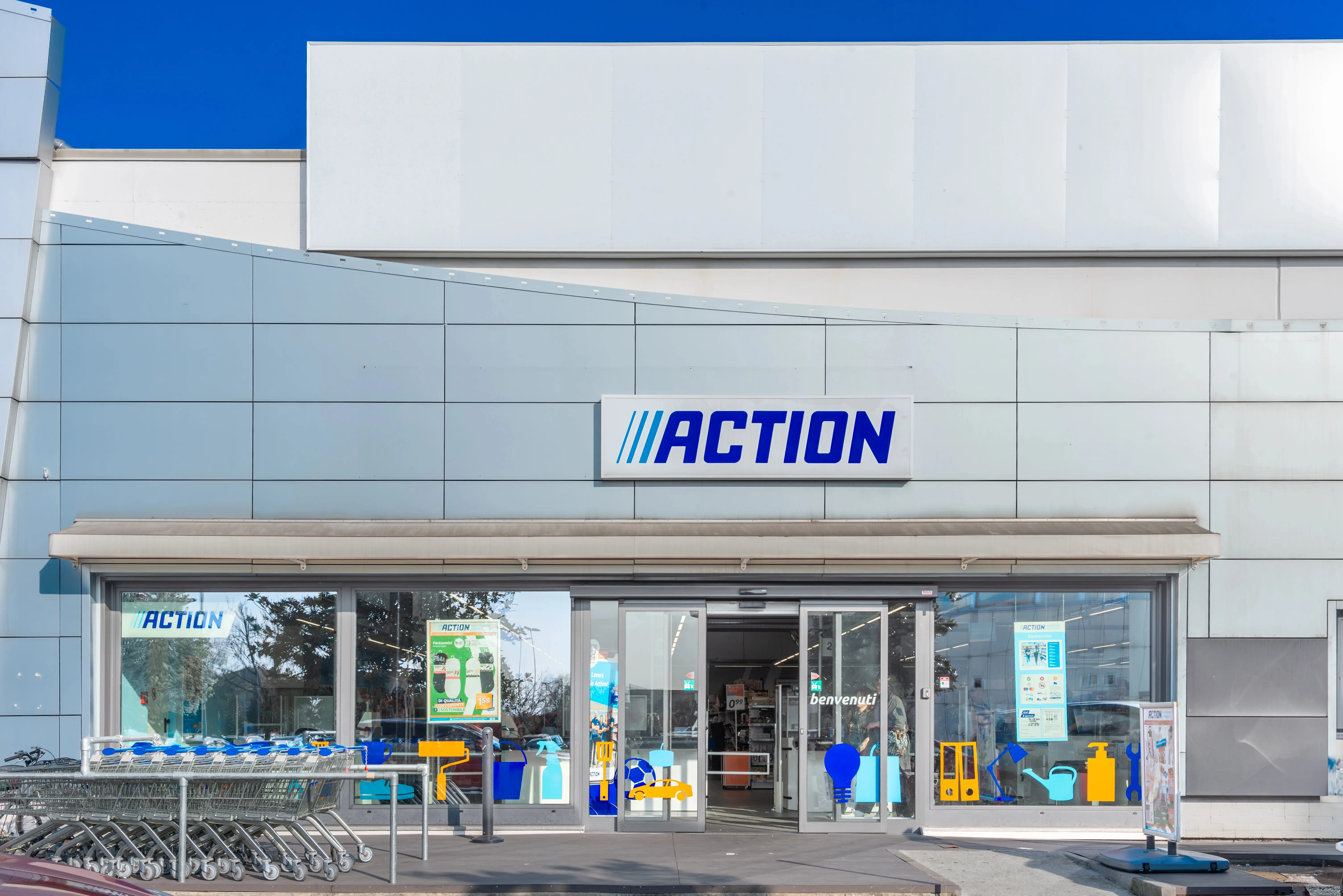 Vstupní část obchodu Action s logem, skleněnými dveřmi a řadou nákupních vozíků