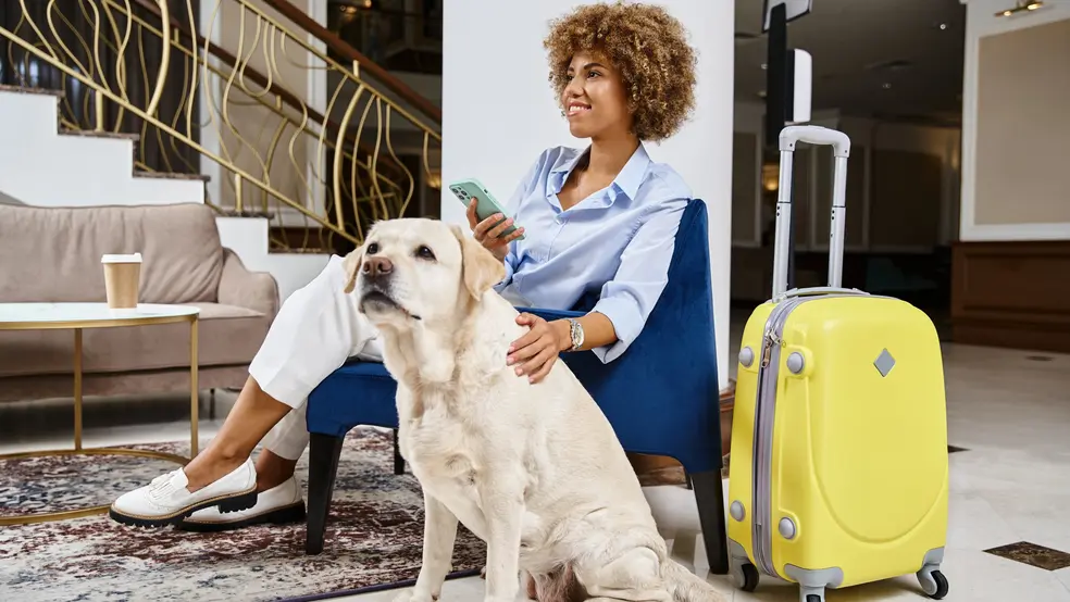 Žena fotí fotoaparátem, zatímco vedle ní leží pes na útesech nad mořem