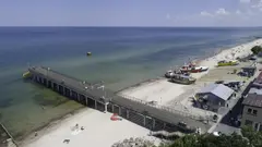Dlouhé molo vedoucí do moře na písčitém pobřeží.
