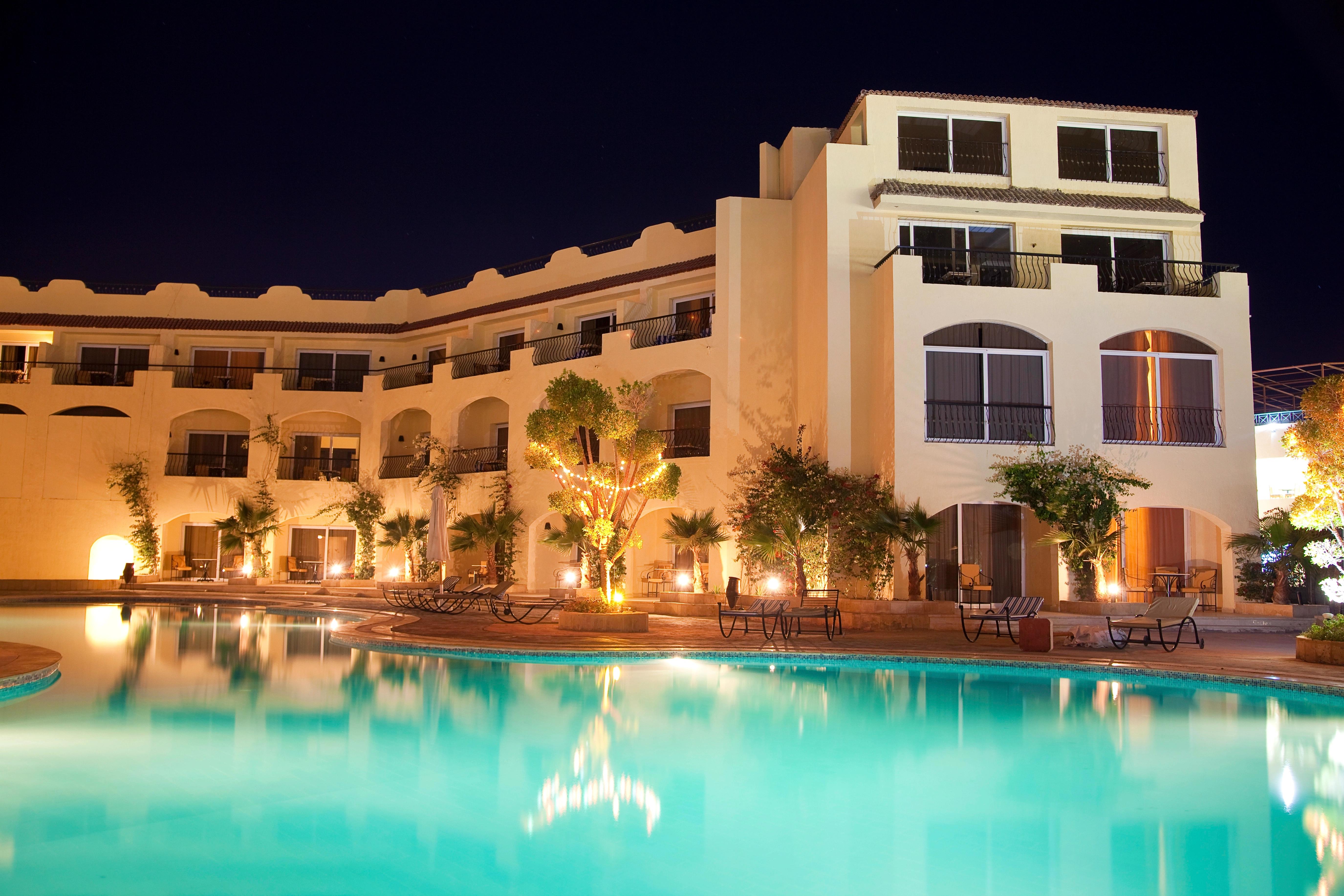 Osvětlený hotelový bazén v noci s lehátky kolem