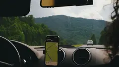 Mobilní telefon s navigační aplikací připevněný v autě, pohled z interiéru na horskou silnici.