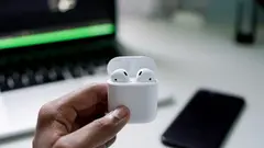 Ruka držící sluchátka AirPods před notebookem MacBook