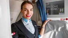 Mladá letuška v uniformě stojí v letadle a usmívá se