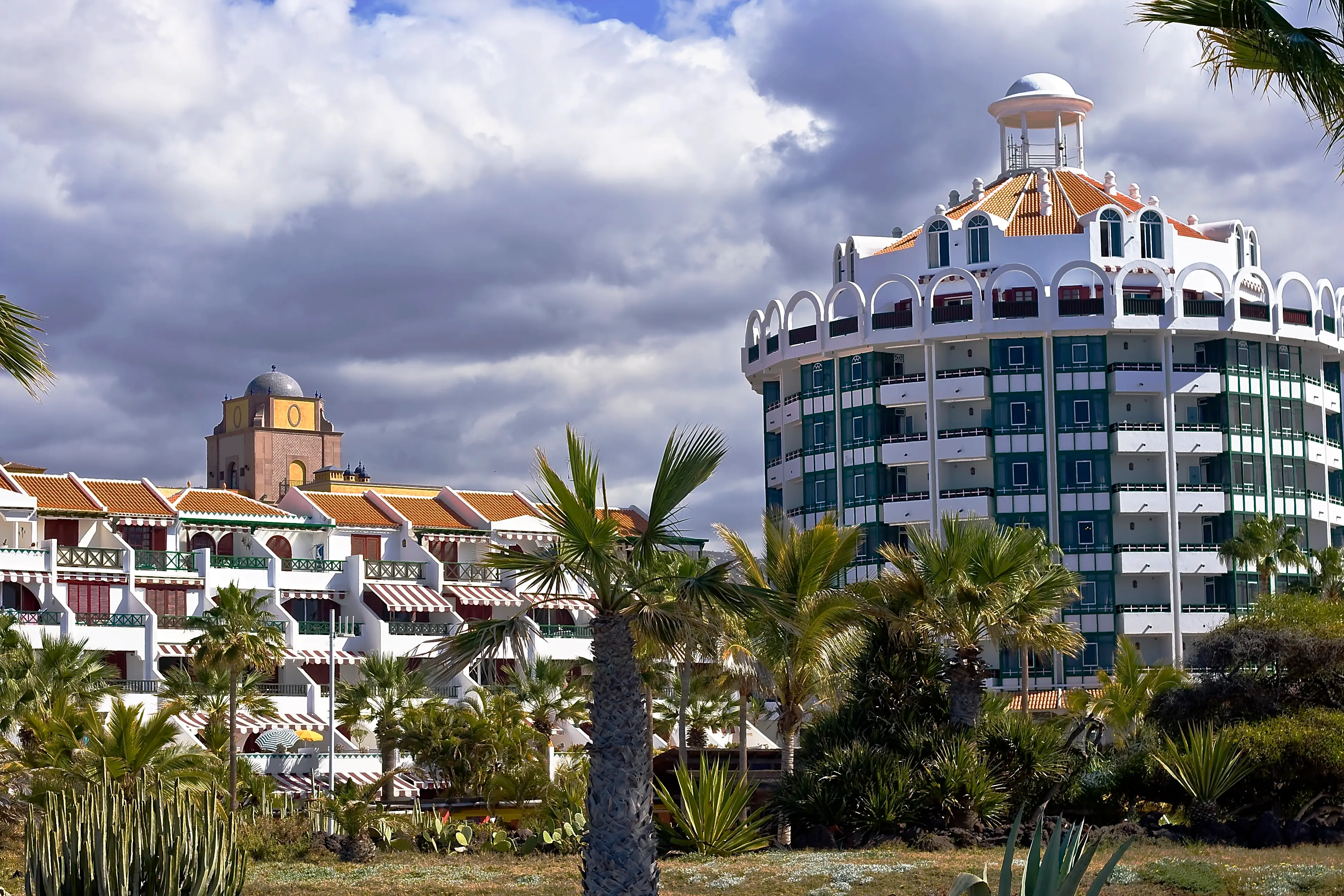 Moderní hotelová budova na Tenerife s palmami v popředí pod zataženou oblohou