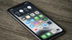 Detailní záběr na domovskou obrazovku iPhonu s různými aplikacemi, položený na dřevěném stole
