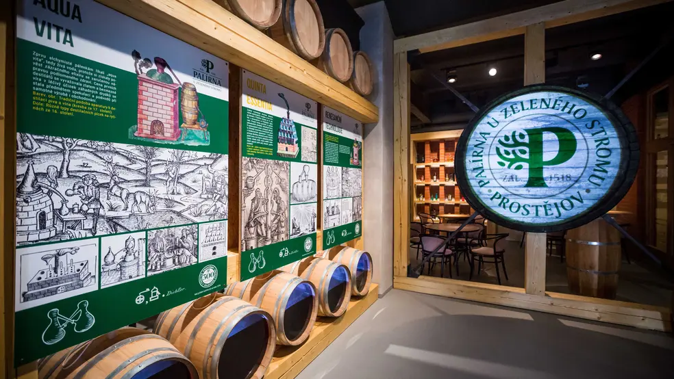 Interiér návštěvnického centra palírny U Zeleného stromu s historickými panely, sudy a projekcí loga