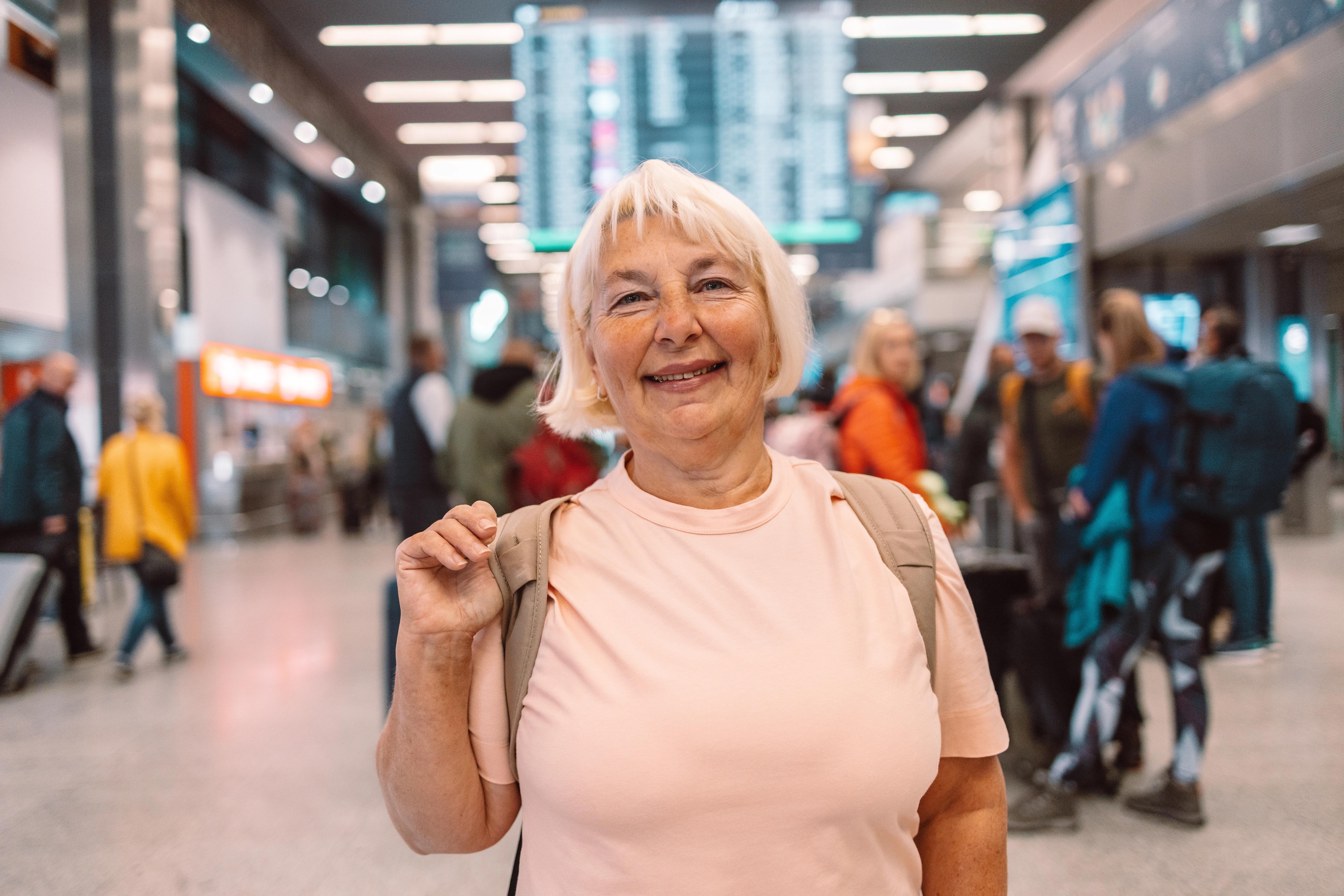 Starší žena s batohem kráčí po nádraží s úsměvem