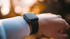 Osoba nosí chytré hodinky, pozadí tvoří rozmazané světlo při západu slunce.