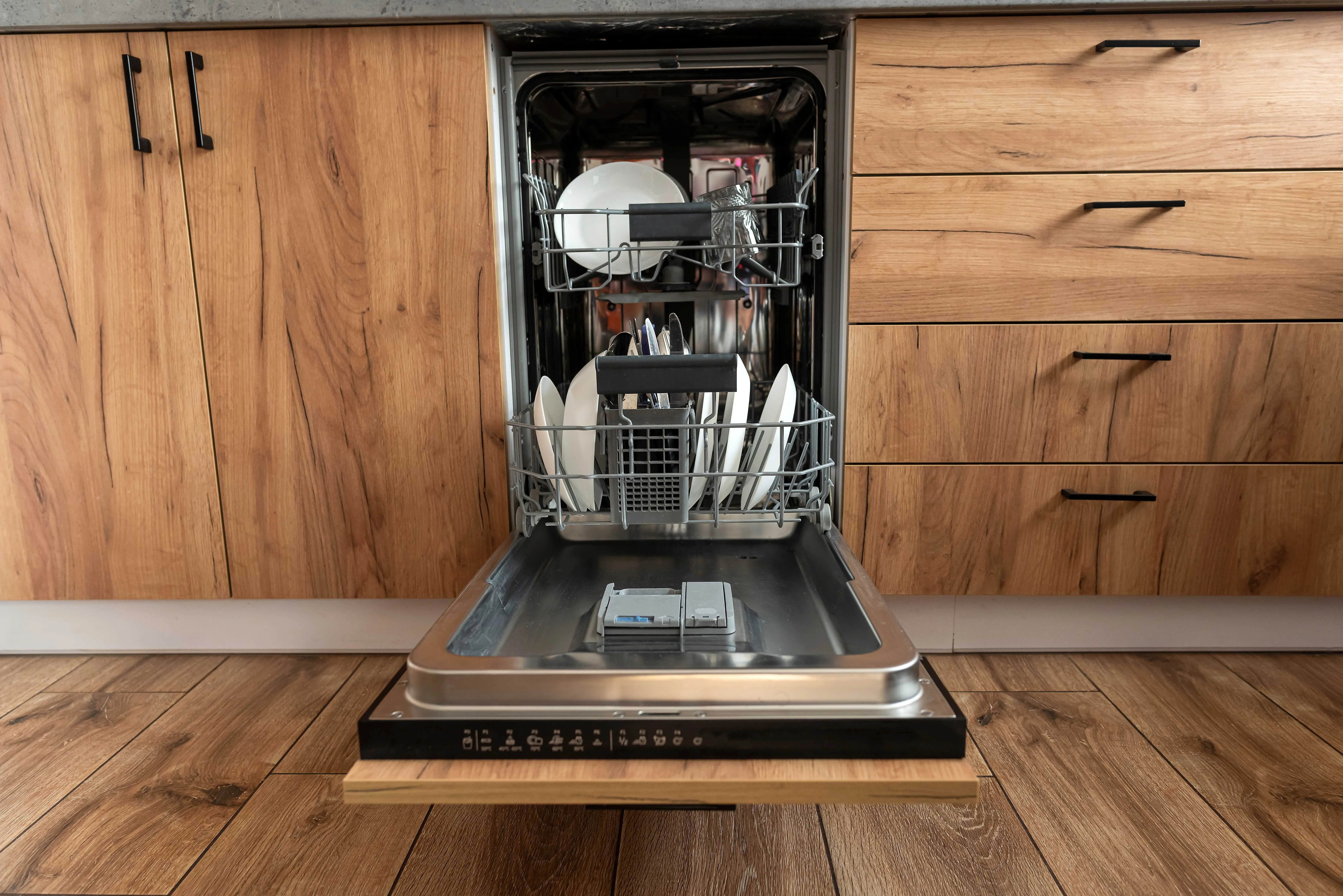 Otevřená myčka nádobí s čistými talíři a příbory po dokončení mycího cyklu