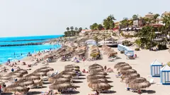 Slunná pláž Playa del Duque na Tenerife s řadami slunečníků a modrobílými kabinkami