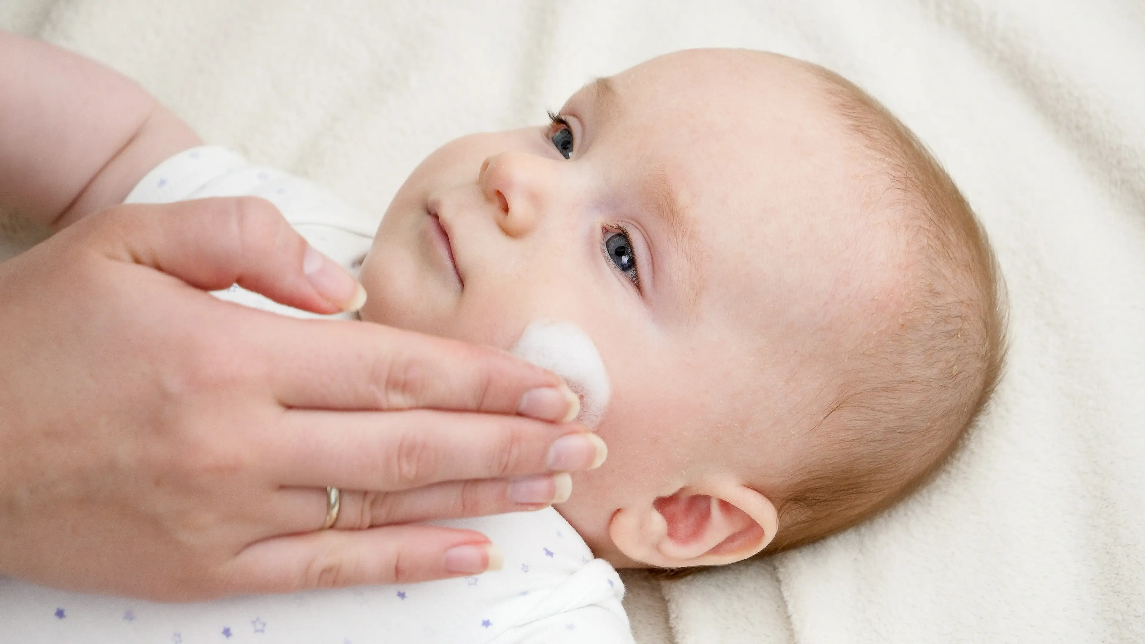 Ruka nanáší krém na nožičku miminka