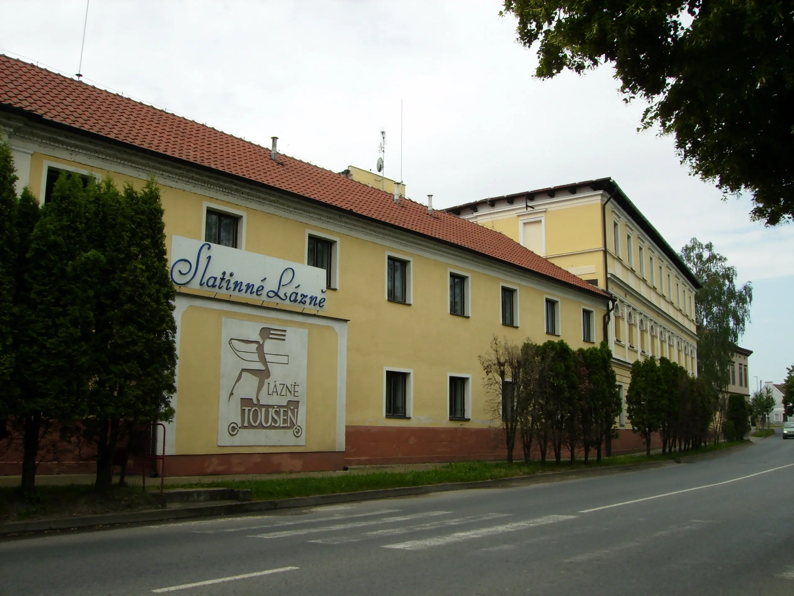 Historická budova lázní v Toušeni s upraveným okolím.