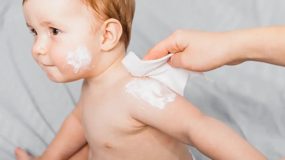 Dětský krém otevřený na přebalovacím pultu vedle plínek