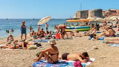 Lidé si užívají slunečný den na pláži Bačvice s výhledem na moře a město Split