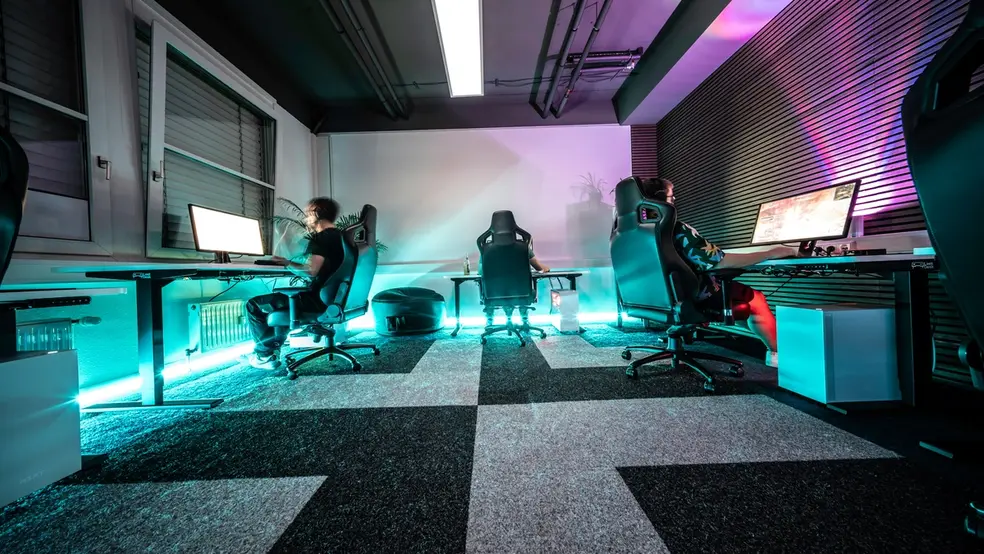 Gamingová místnost s barevným osvětlením a herními stanicemi.