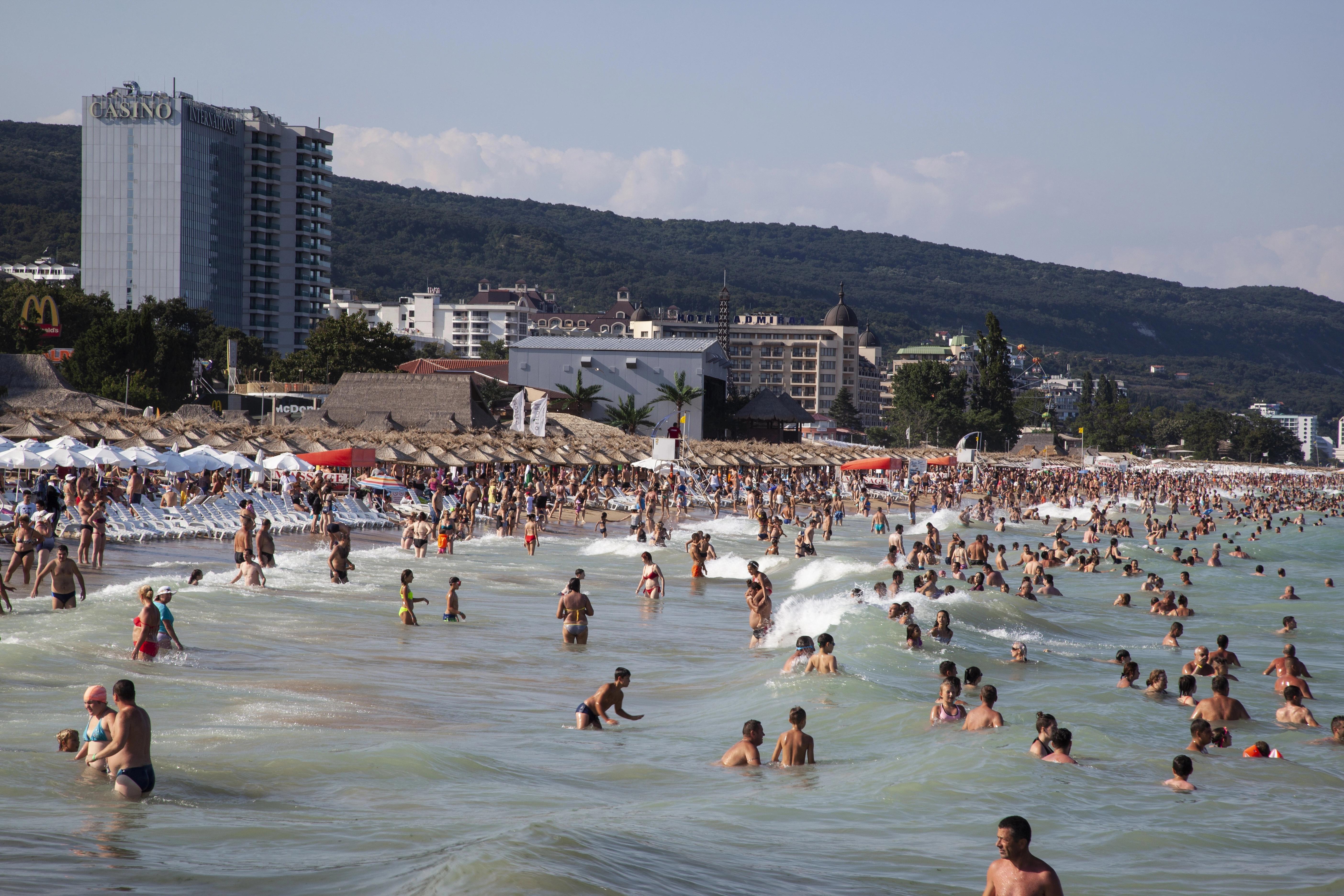 Davy lidí v moři a na pláži u hotelů a kasina ve Zlatých píscích, v pozadí zalesněné kopce