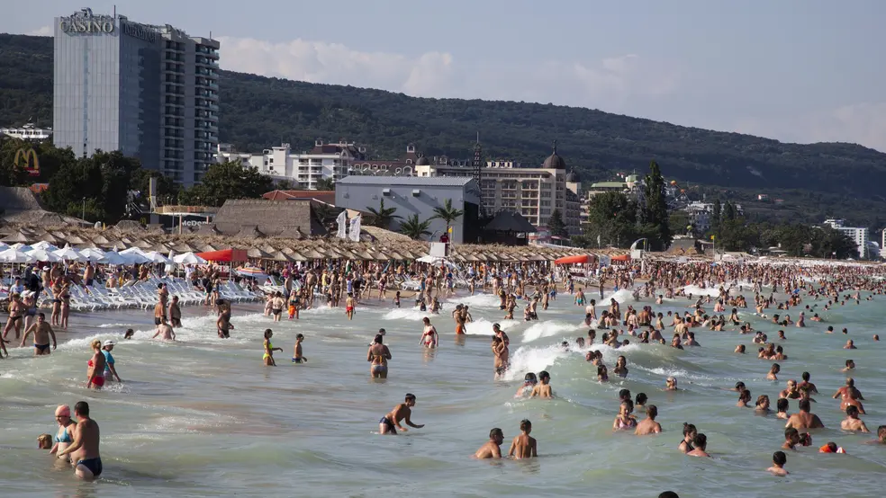 Davy lidí v moři a na pláži u hotelů a kasina ve Zlatých píscích, v pozadí zalesněné kopce