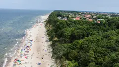 Letecký pohled na pláž s turisty a lesem v pozadí,