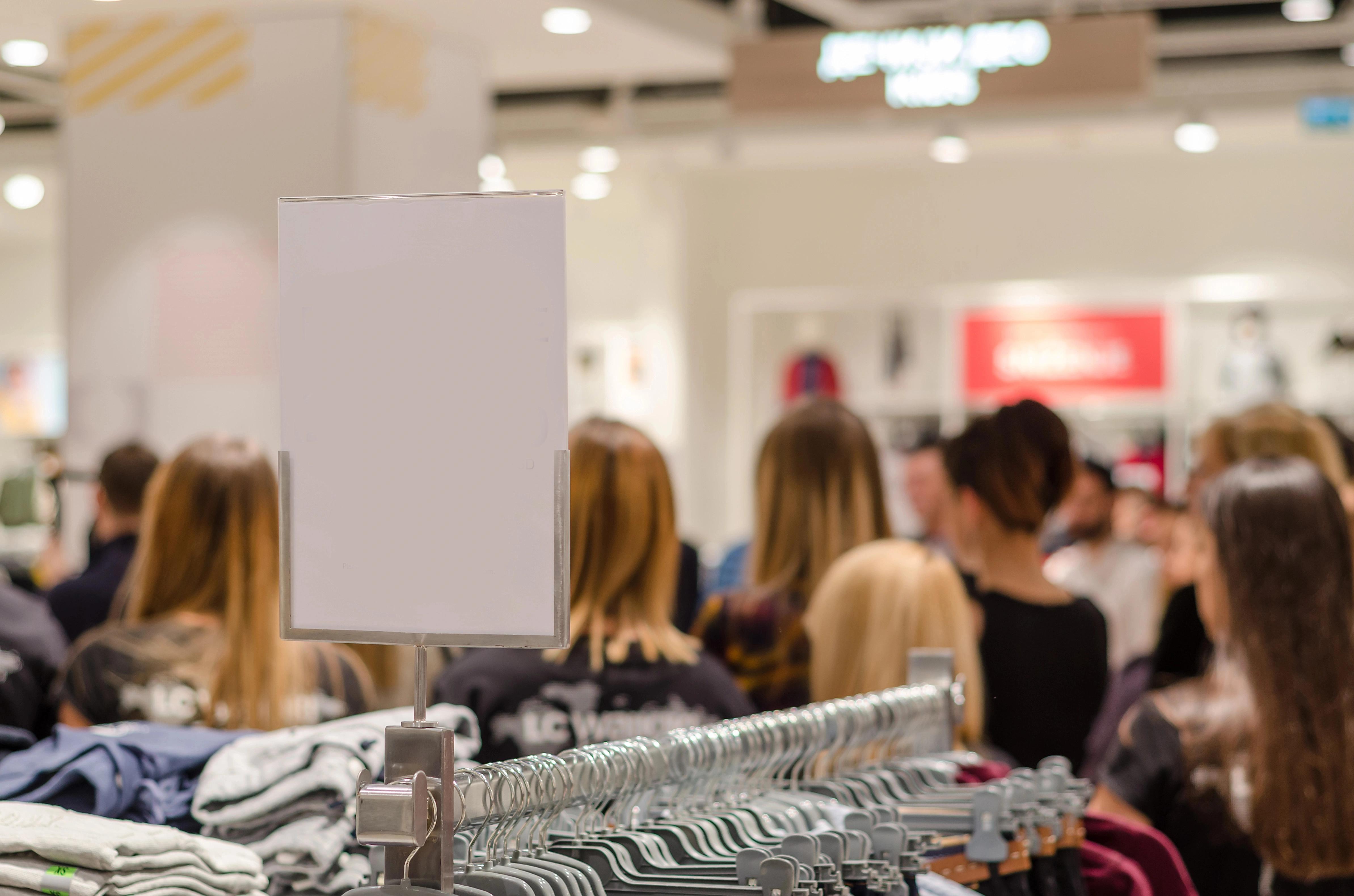 Detail věšáků s oblečením a rozmazané postavy zákazníků v pozadí