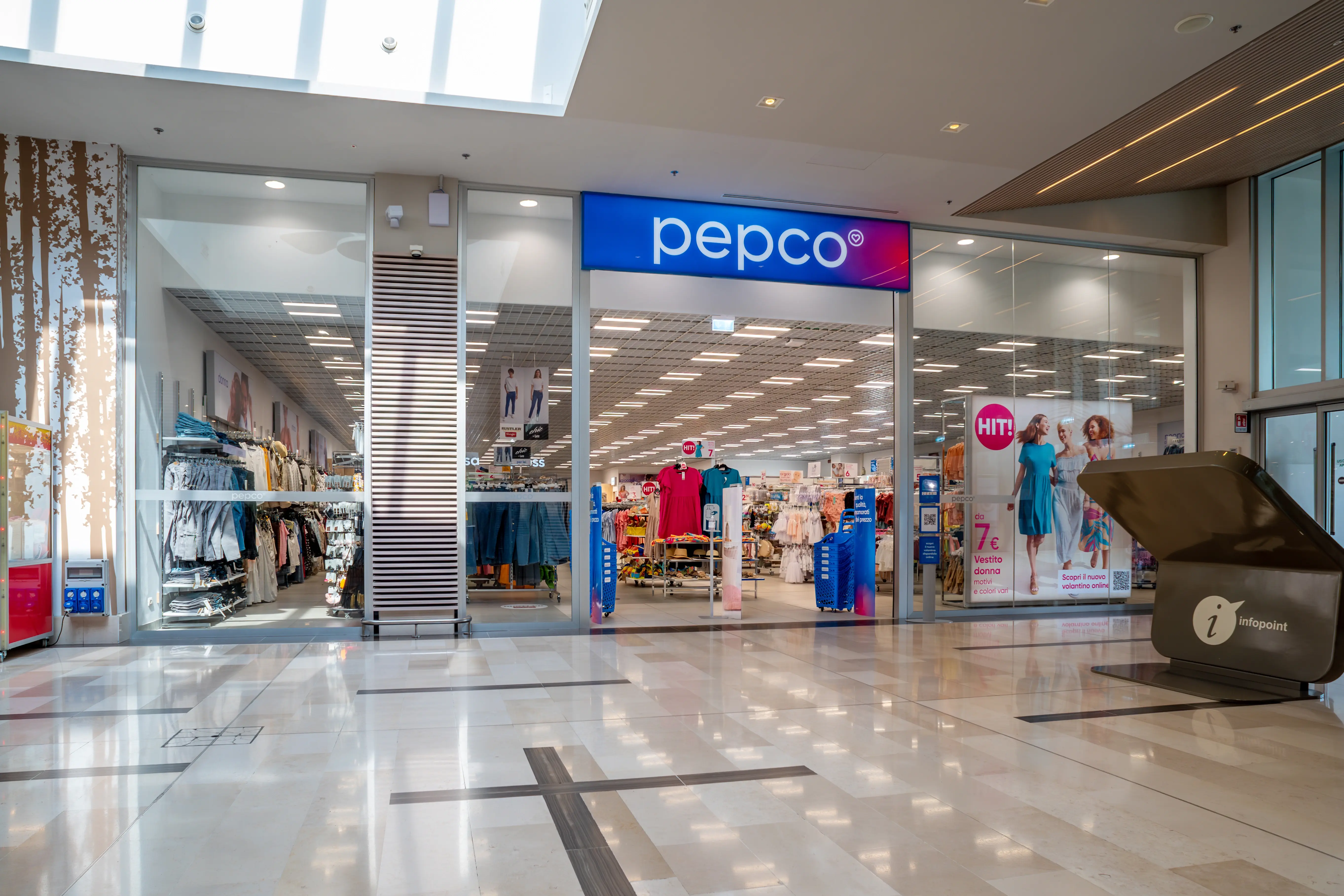 Vchod do obchodu Pepco s prosklenou fasádou, uvnitř regály s oblečením a domácími potřebami