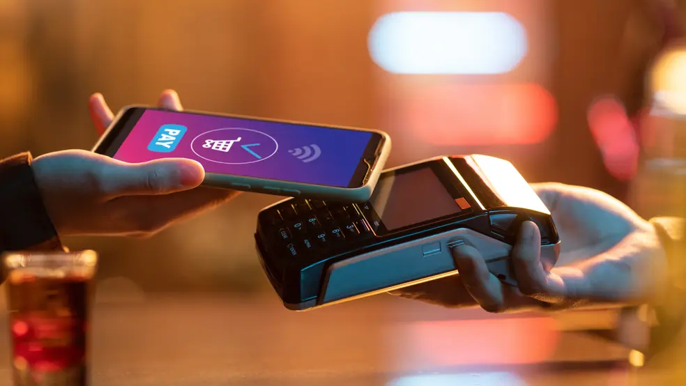 Ruka držící mobil s otevřenou platební aplikací před terminálem