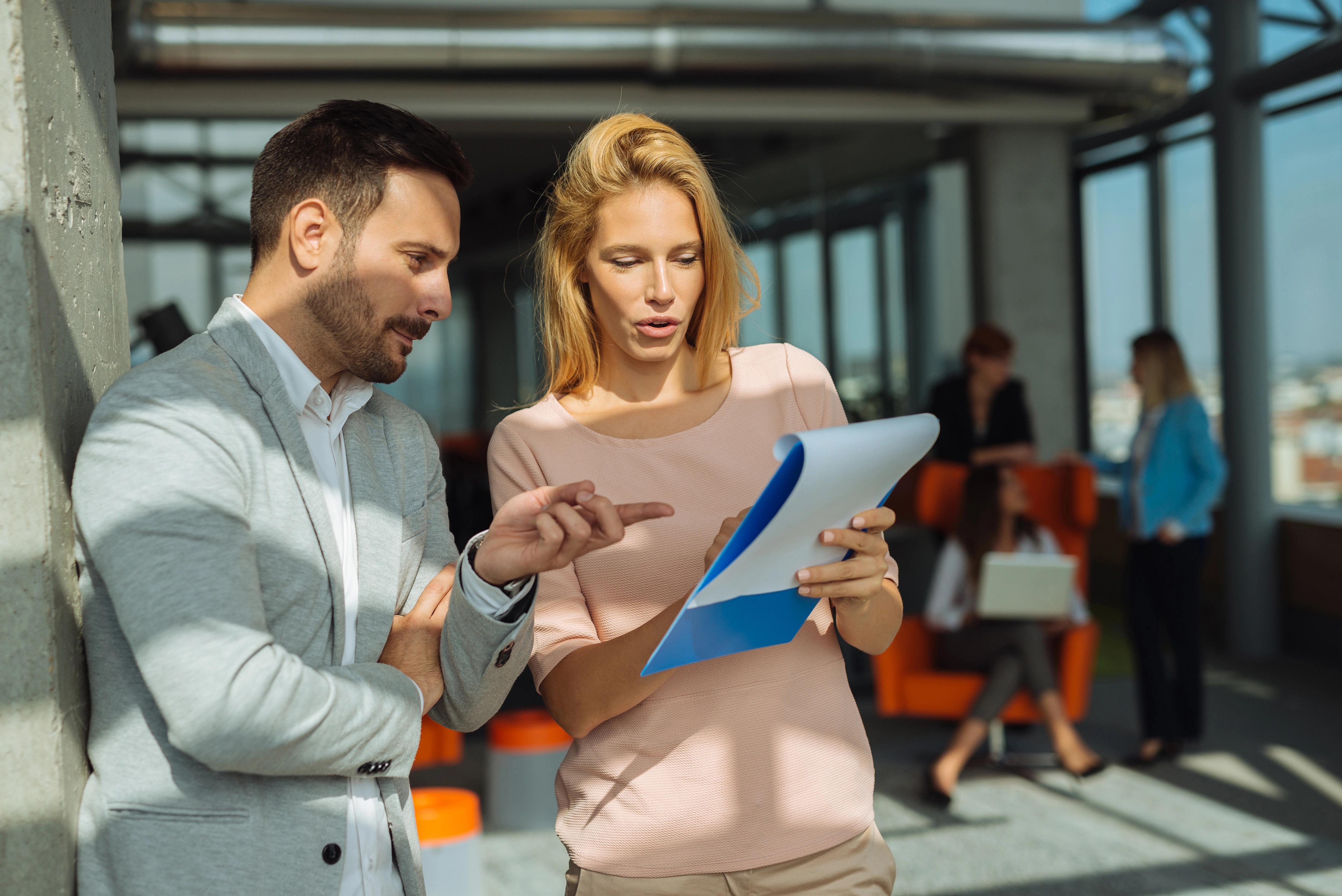 Muž a žena v moderní kanceláři procházejí dokumenty a diskutují nad nimi.