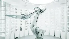 Robotické rameno v moderní laboratoři obklopené skleněnými stěnami s úložnými boxy.