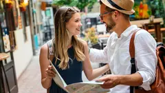 Mladý pár stojí v ulici a prohlíží si papírovou mapu