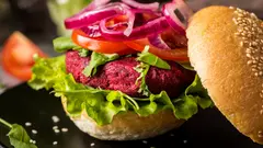 Ruka držící hamburger s rozkrojenou houskou a masem