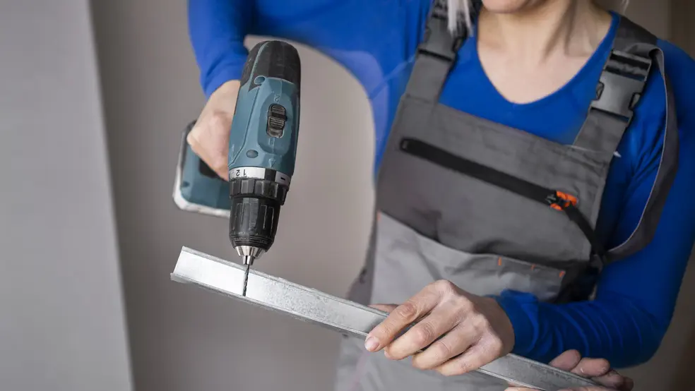 Elektrická vrtačka na stole vedle kufříku s příslušenstvím