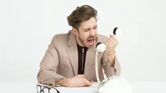 Muž křičící do starého telefonu na bílém pozadí