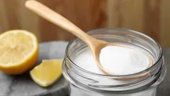 Dřevěná lžička s jedlou sodou v otevřené sklenici, vedle nakrájeného citronu