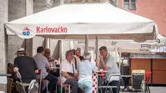 Hosté sedí u stolů před kavárnou v Chorvatsku.