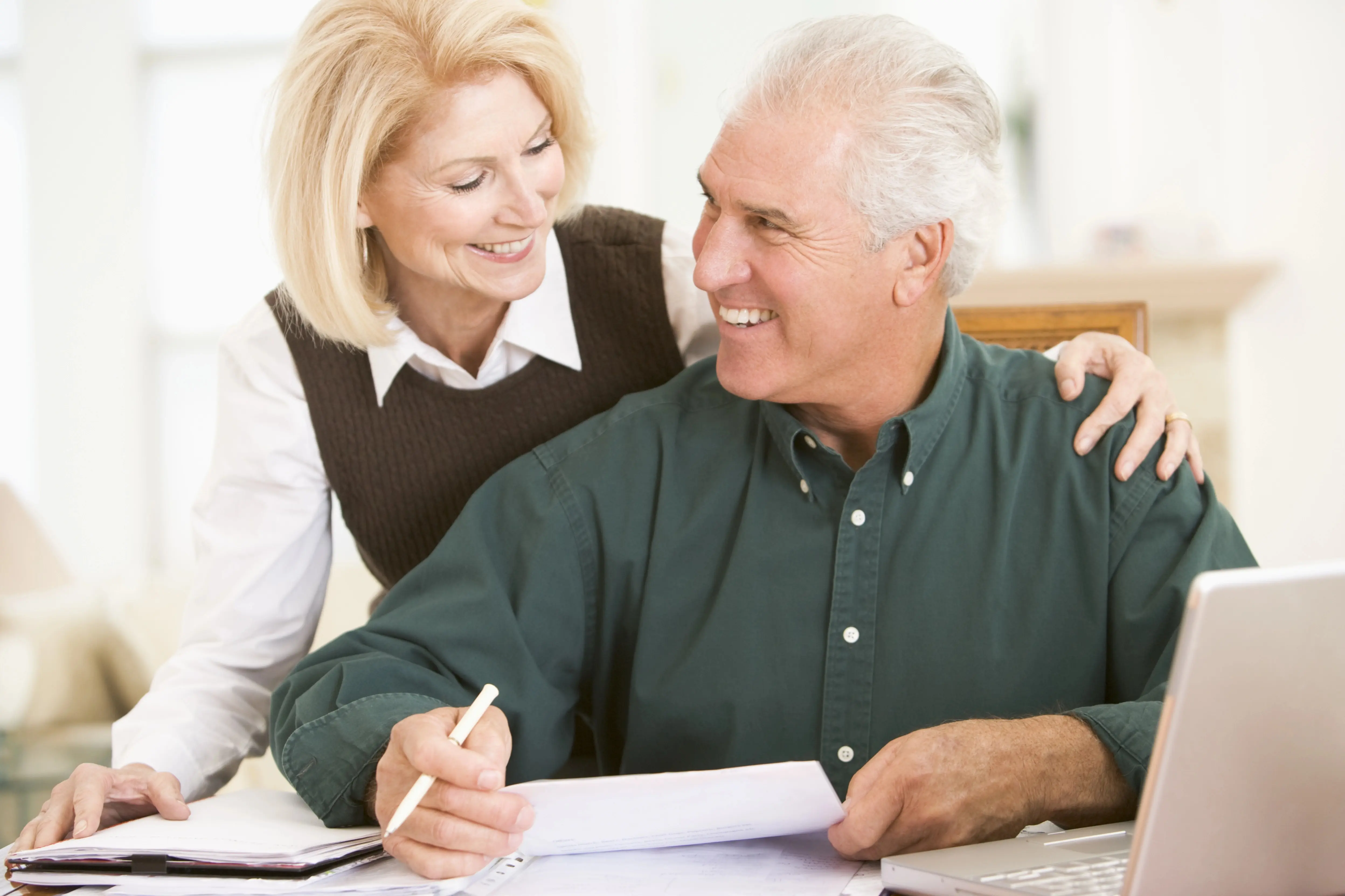 Starší žena v obýváku vkládá minci do oranžového prasátka, v ruce drží účet